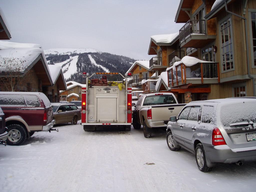 A fire truck on a narrow street with cars parked on the right and left
